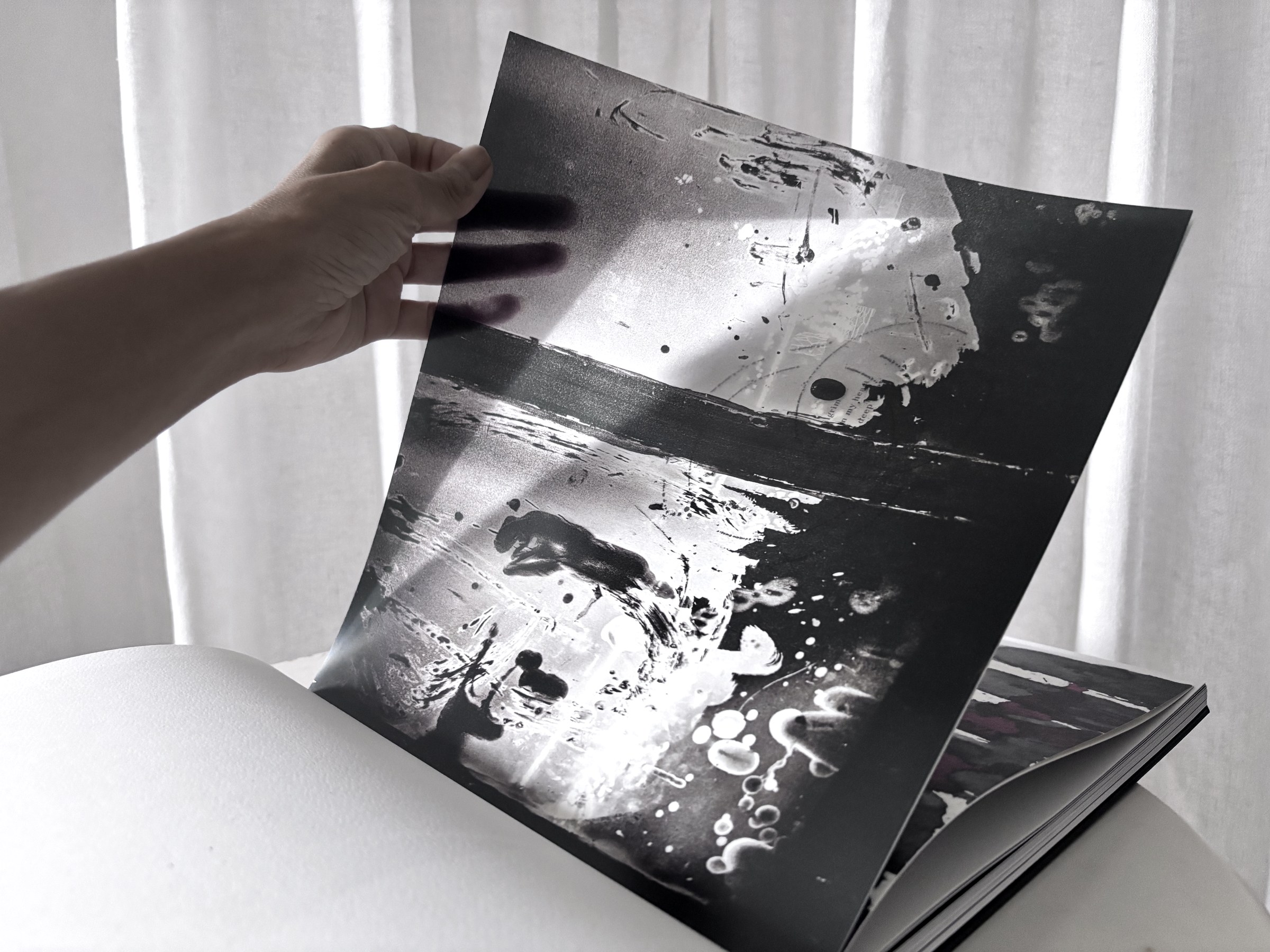 A hand lifting a printed page mid-turn, the fingers showing through from behind as light passes through the paper