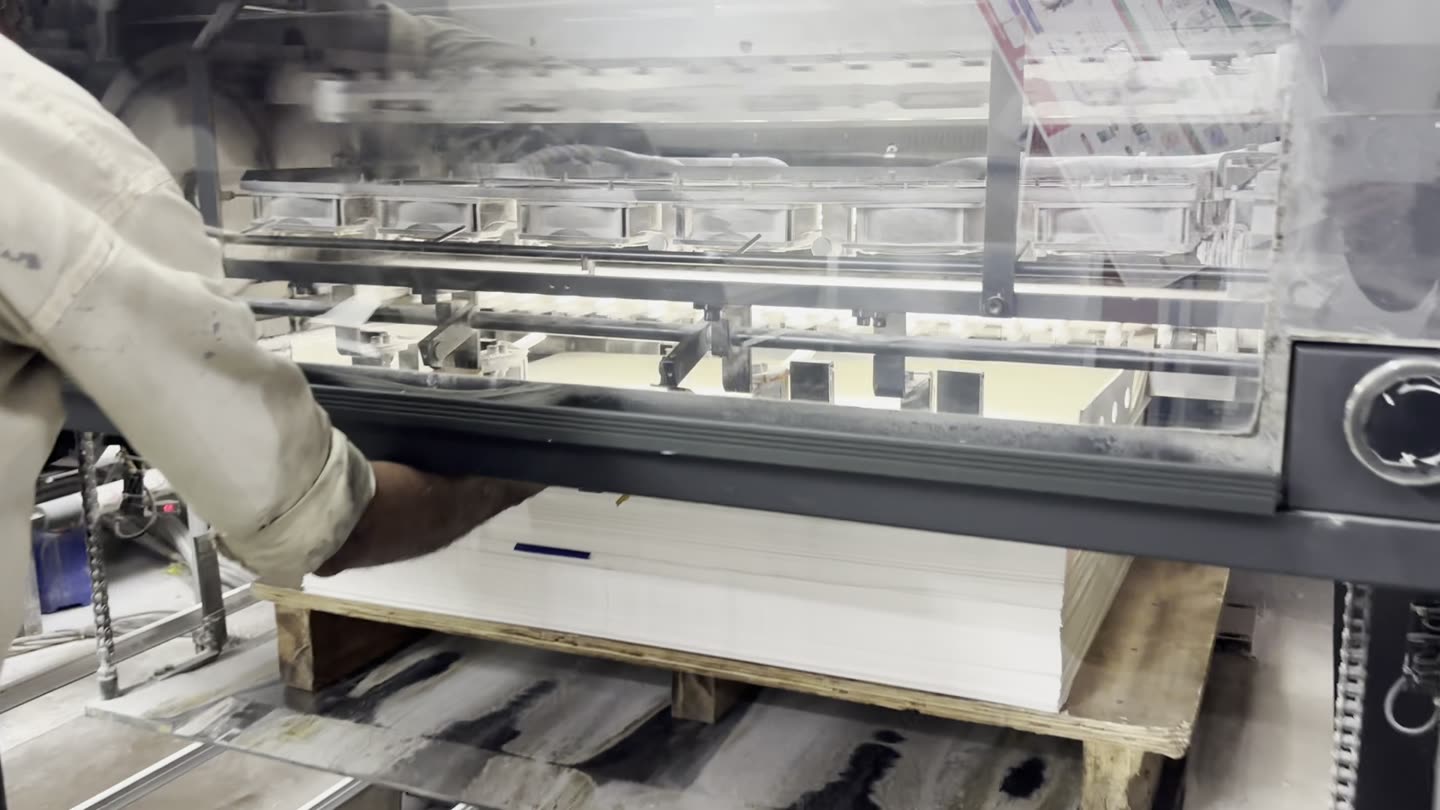 Hands feeding a large sheet of paper into an offset press